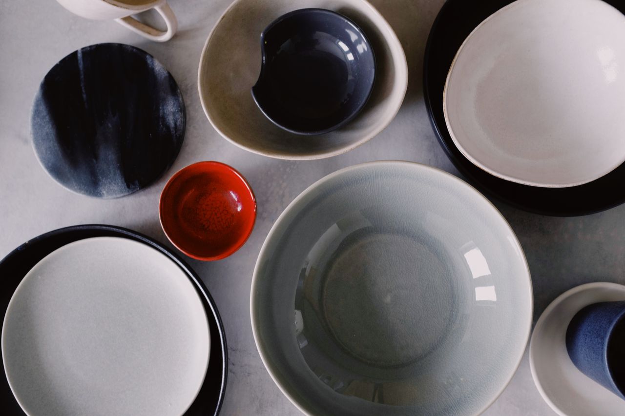 who-we-are A collection of various colored ceramic bowls and plates, artistically arranged on a flat surface.