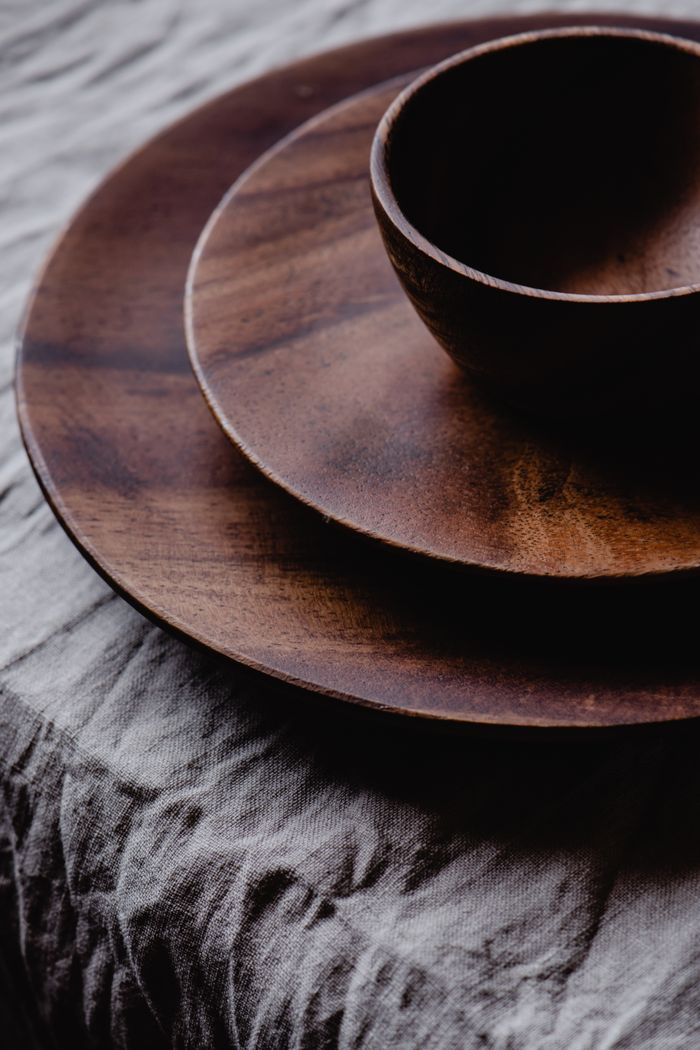 Close-up of a rustic wooden bowl and plate set on a textured fabric surface, showcasing natural elegance.