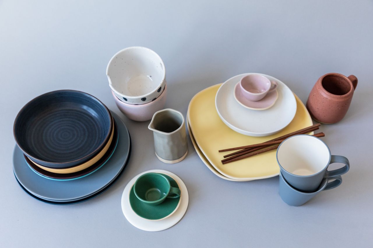 A diverse collection of ceramic tableware including plates, mugs, bowls, and cups on a blue surface.